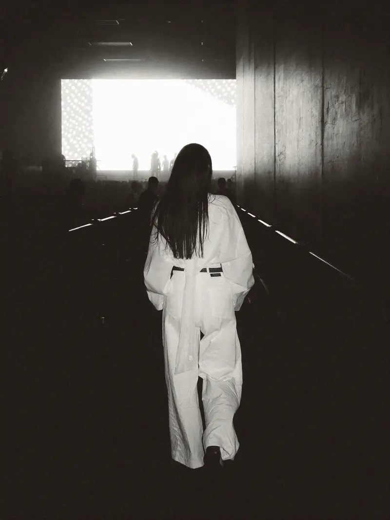 A performer in a white suit walking towards a bright stage